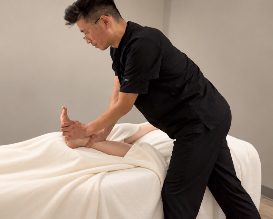 A practitioner stretching a person's foot and ankle on the treatment table