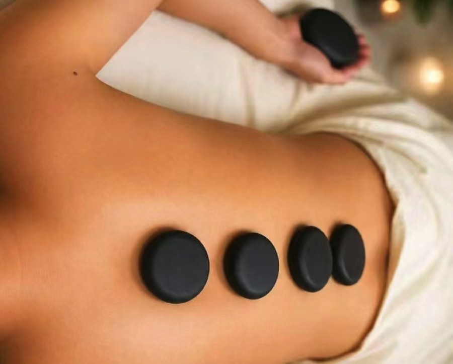 Four hot stones resting along a person's back while a therapist holds another